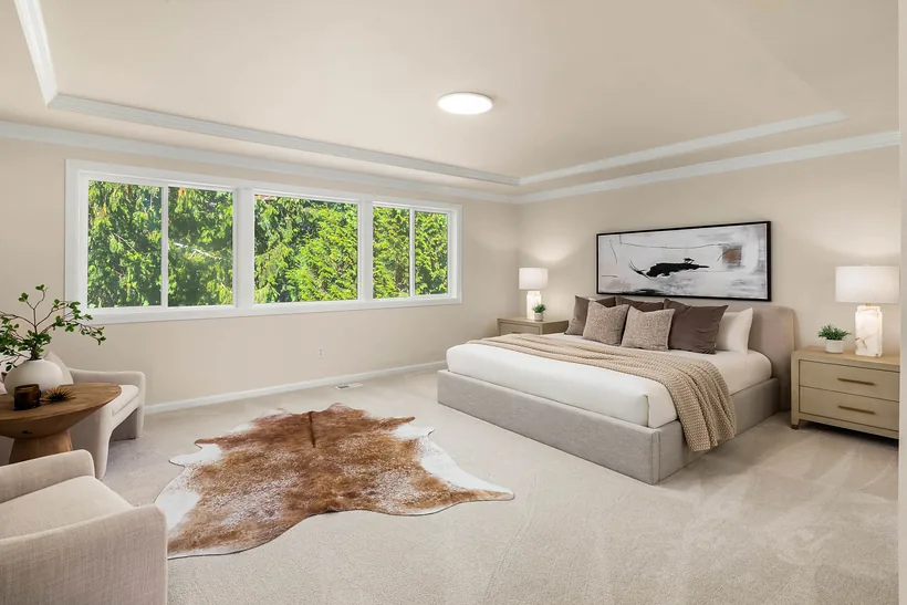 Primary suite with a tray ceiling, a sitting area and a wall of windows facing the trees