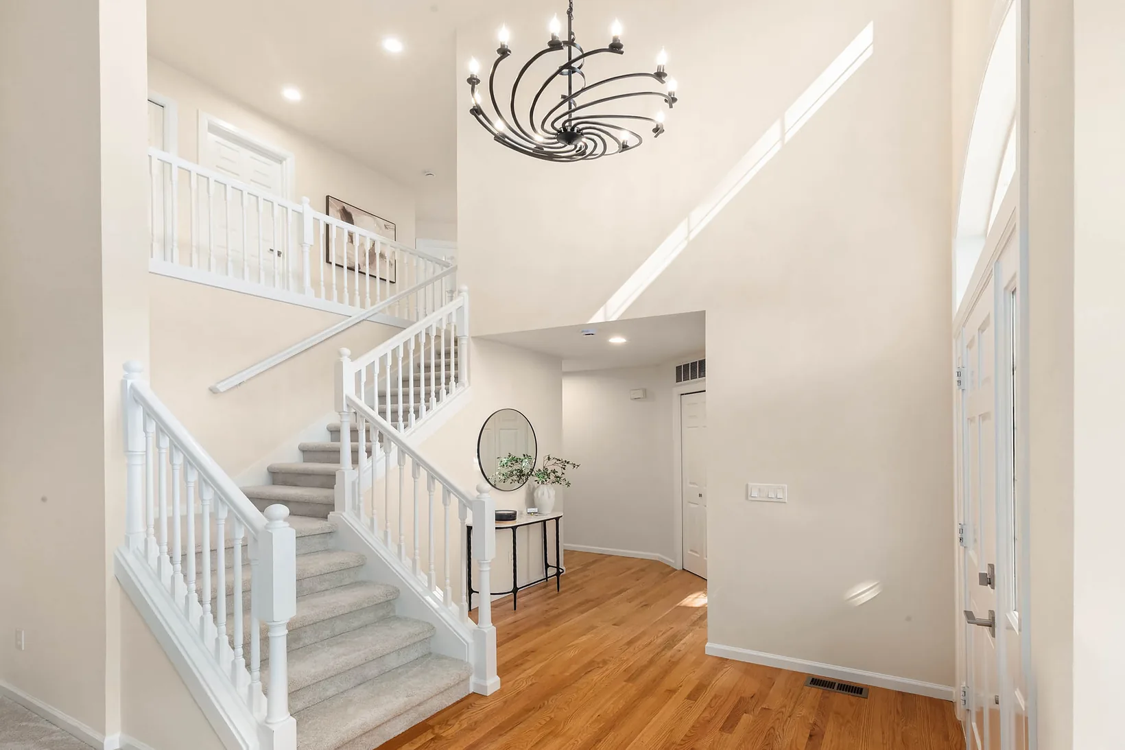 Two-story foyer with hardwood floors, a curved staircase and a black iron chandelier